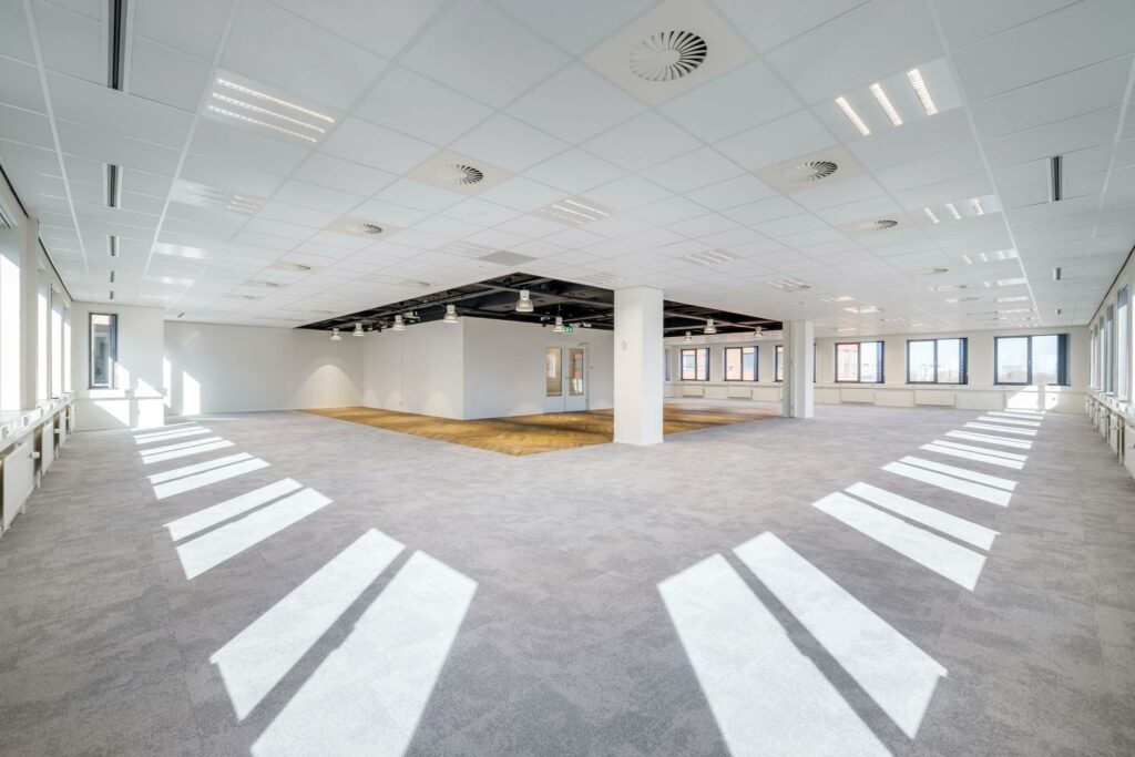 Licht en ruim kantoorpand aan de Karspeldreef met grijs tapijt, systeemplafond en grote ramen.