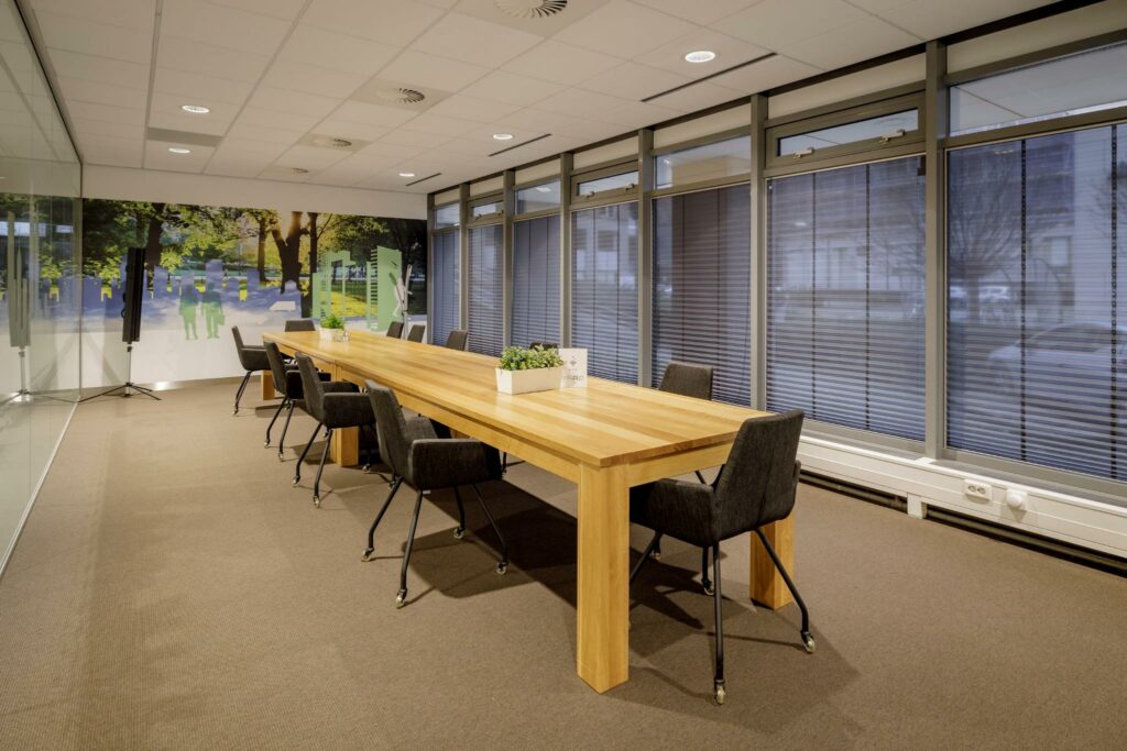 Vergaderruimte aan de Karspeldreef met een lange houten tafel, zwarte stoelen en een kleurrijke wanddecoratie met stads- en natuurelementen.