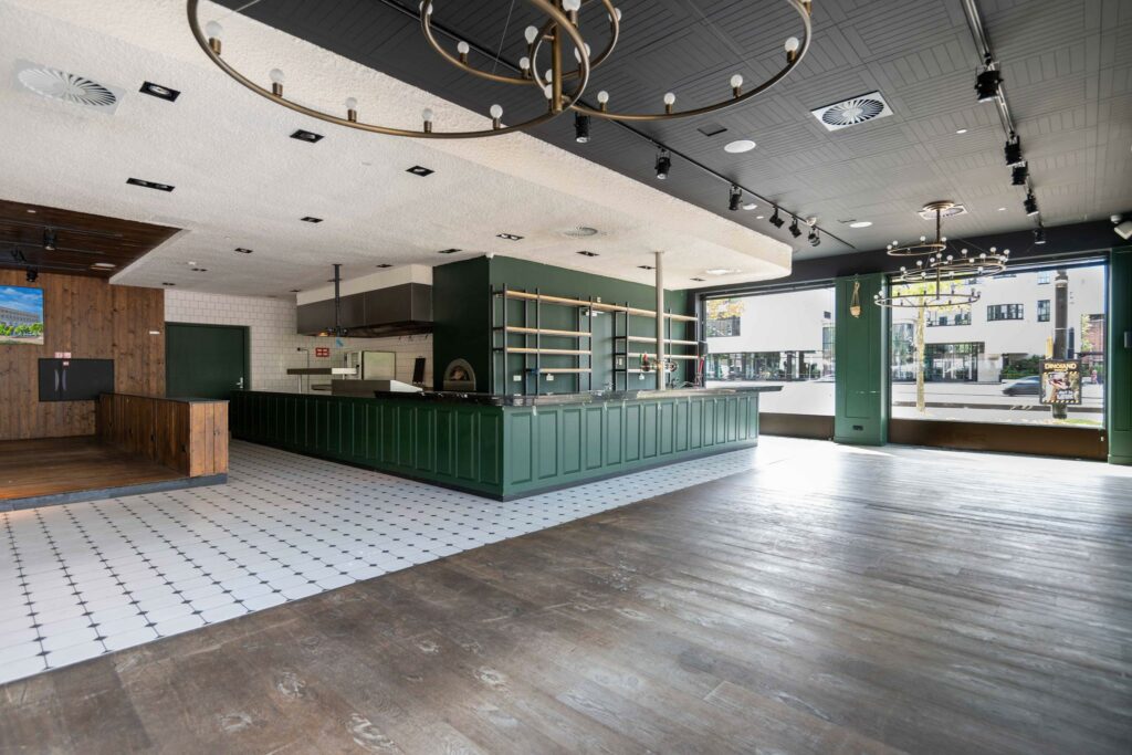 Modern, leeg restaurantinterieur aan het Stadionplein met een open keuken, groene bar en grote ramen aan de straatzijde.