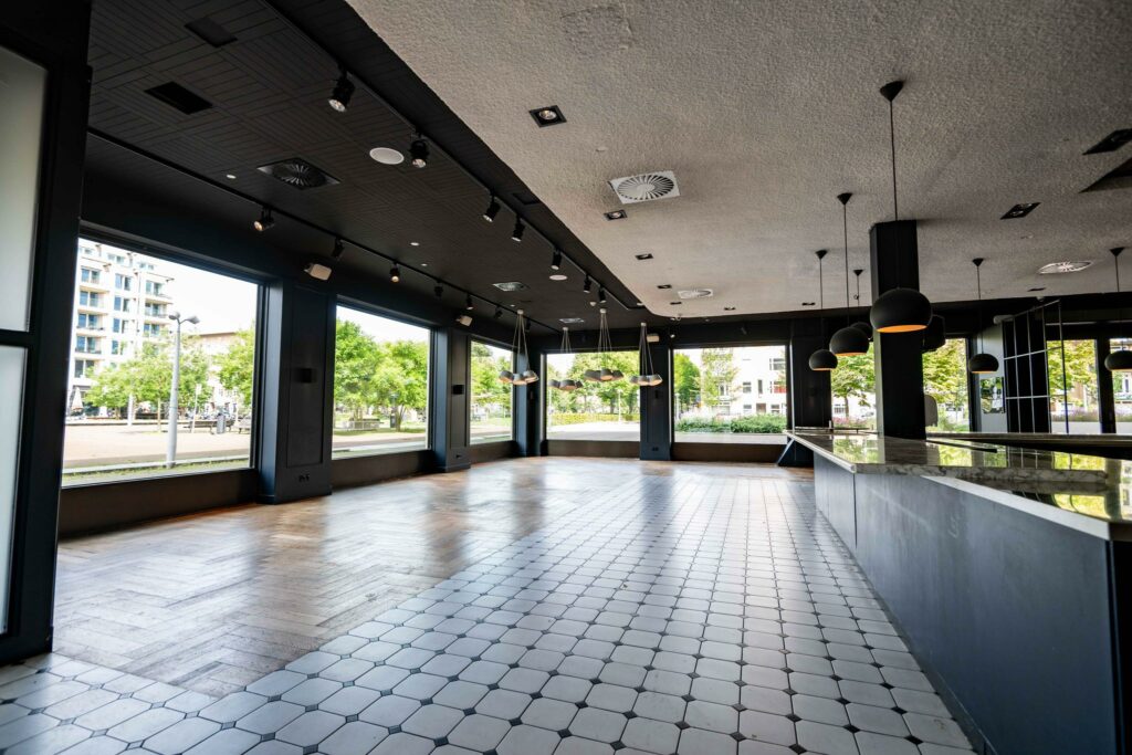Licht en modern interieur van een leeg horecapand aan het Stadionplein met grote ramen en een betegelde vloer.