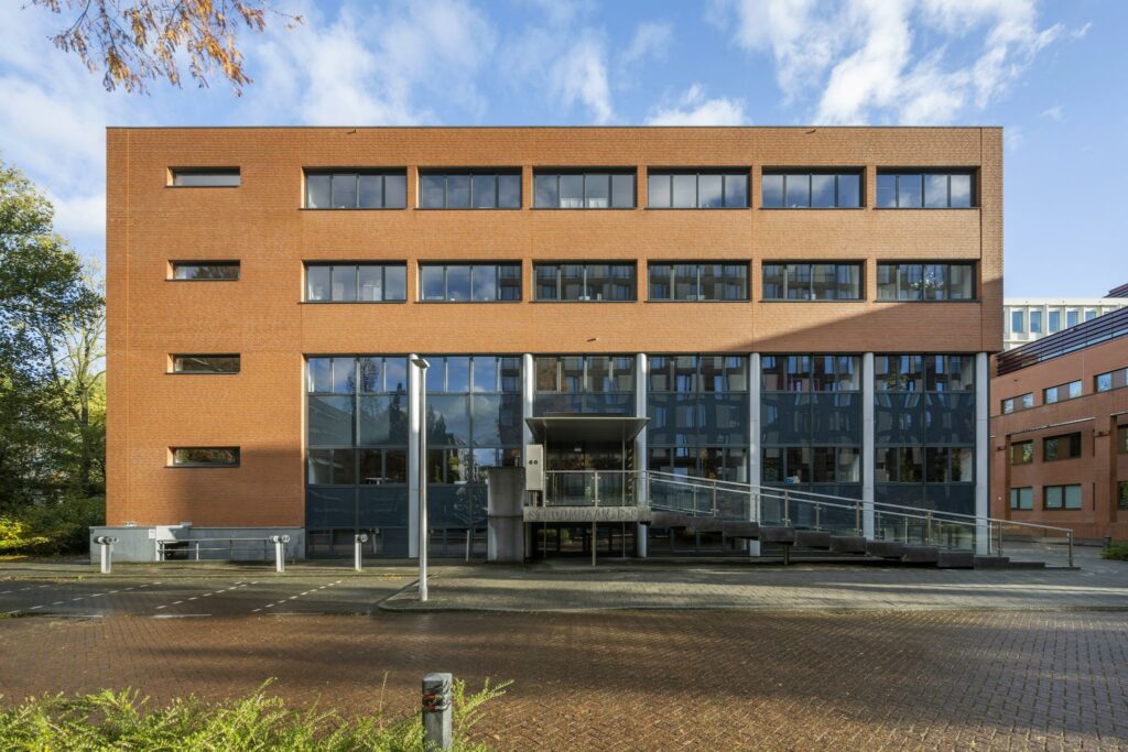 Voorzijde van het kantoorgebouw aan de Stroombaan 4–6 met rode bakstenen gevel en glazen entreepartij.