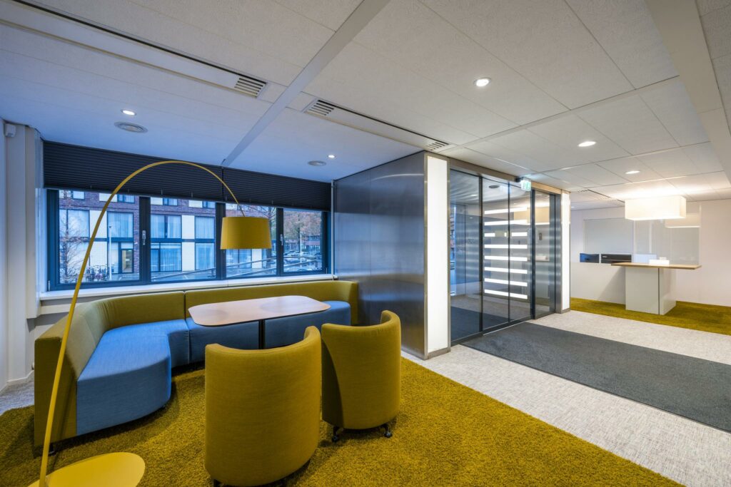 Moderne kantoorruimte met kleurrijke zithoek, gele accenten en glazen entree bij Stroombaan.