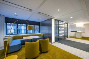 Moderne kantoorruimte met kleurrijke zithoek, gele accenten en glazen entree bij Stroombaan.
