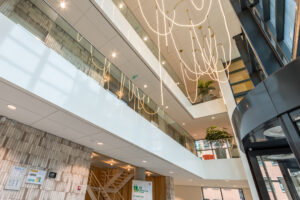 Moderne lobby van een kantoorpand aan de Hullenbergweg met glazen balustrades, hangende lichtinstallatie en groene planten.