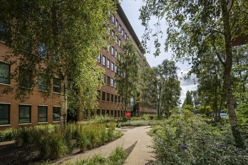 Kantoorgebouw aan de Hullenbergweg omgeven door een groene tuin met wandelpad en bomen.