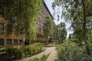 Kantoorgebouw aan de Hullenbergweg omgeven door een groene tuin met wandelpad en bomen.