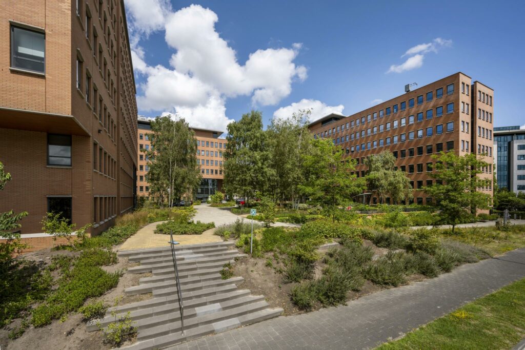 Kantoorgebouwen aan de Hullenbergweg met een groene binnentuin en looppaden onder een blauwe hemel.