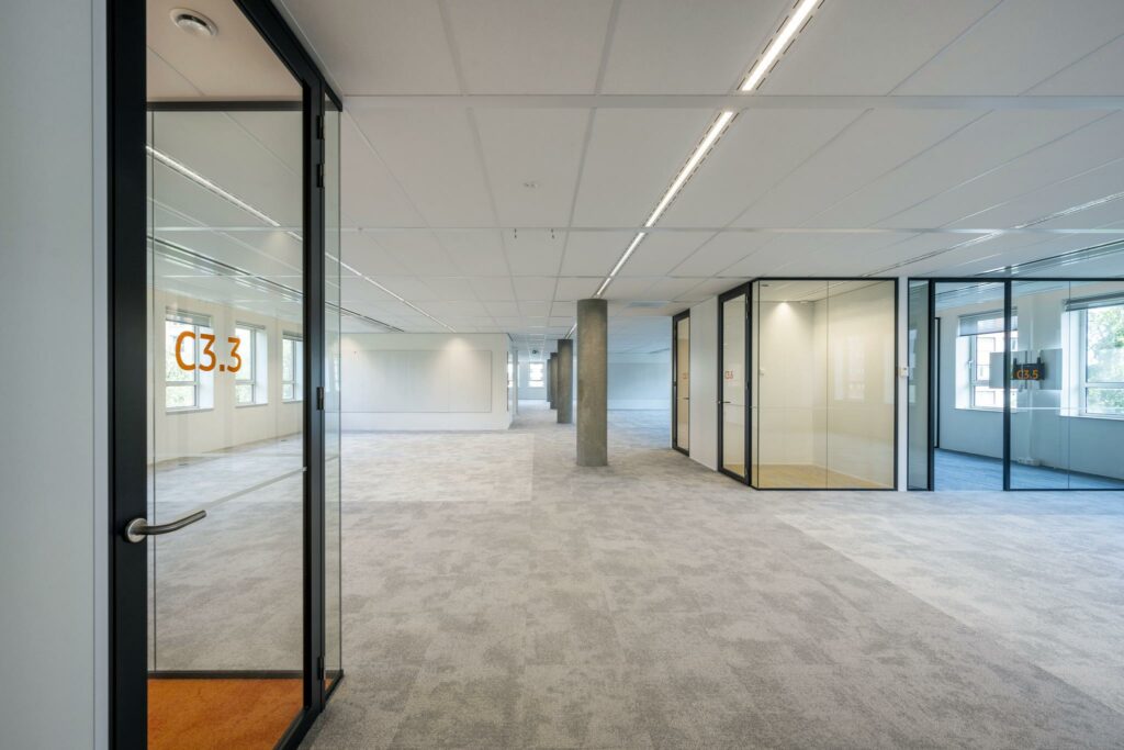 Moderne, lege kantoorruimte aan de Hullenbergweg met glazen vergaderruimtes en neutraal tapijt.