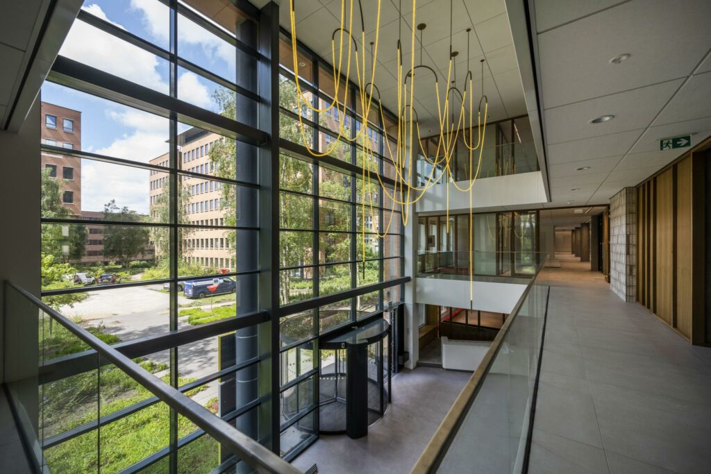 Moderne kantoorlobby aan de Hullenbergweg met glazen gevel, gele hangverlichting en uitzicht op omliggende kantoorpanden.