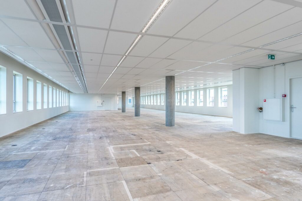 Leeg en licht kantoorpand aan de Hullenbergweg met grote raampartijen en betonnen vloer.