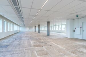 Leeg en licht kantoorpand aan de Hullenbergweg met grote raampartijen en betonnen vloer.