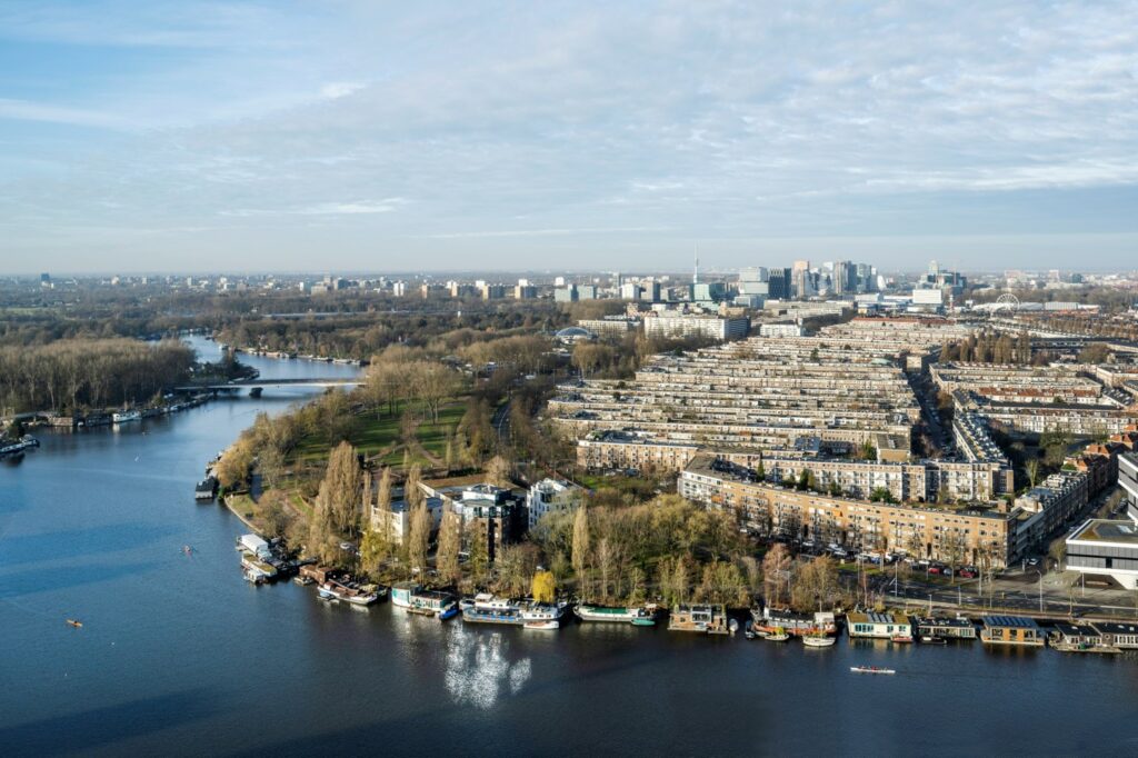 Luchtfoto van Amstelplein in Amsterdam met woonboten, parken en de skyline van de Zuidas op de achtergrond.