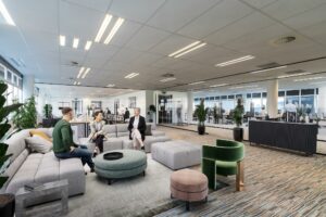 Moderne kantoorlounge aan de Lemelerbergweg met drie personen in gesprek en werkplekken op de achtergrond.