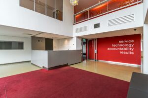 Moderne ontvangsthal van een kantoorpand aan de Lemelerbergweg met rode accenten en de kernwaarden “service, technology, accountability, results” op de muur.