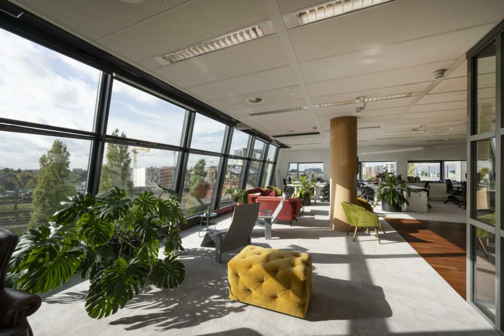 Moderne kantoorruimte op Rietlandpark met grote ramen, veel daglicht, planten en kleurrijke zitmeubels.