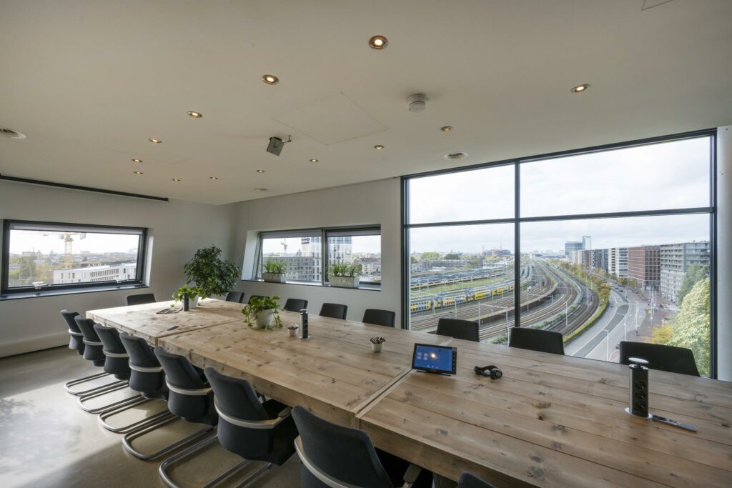 Vergaderruimte met een grote houten tafel en uitzicht op het spoor bij het Rietlandpark in Amsterdam.
