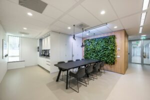 Moderne vergaderruimte aan de Paalbergweg met een lange tafel, groene plantenwand en geïntegreerde kitchenette.