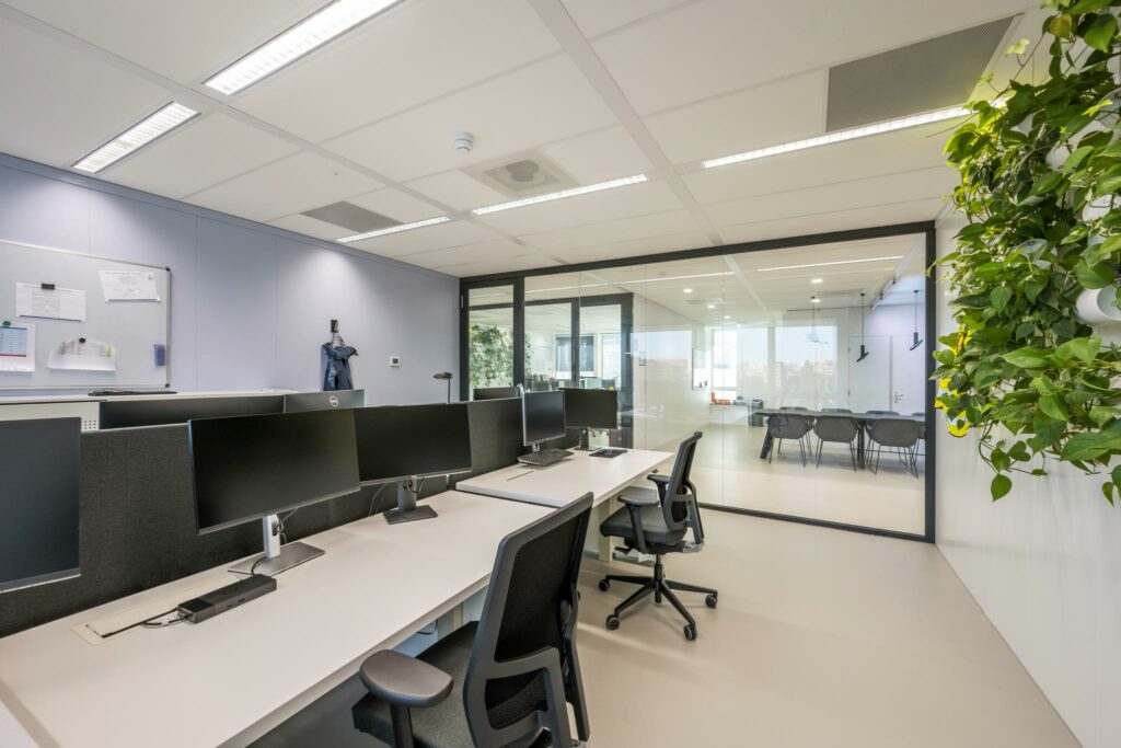 Moderne open kantoorruimte aan de Paalbergweg met werkplekken, glazen vergaderruimte en groene wanddecoratie.