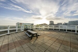 Ruimtelijk dakterras aan de Paalbergweg met picknicktafels, glazen balustrade en uitzicht op moderne gebouwen bij zonsopkomst.