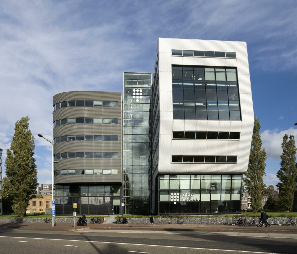 Modern kantoorgebouw van Taipa Network aan het Rietlandpark in Amsterdam met opvallende glazen en witte gevel.