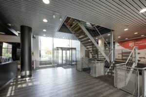 Moderne entreehal van het kantoorgebouw Rietlandpark met glazen deuren, houten trap en metalen accenten.