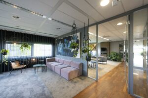 Modern ingerichte loungeruimte in kantoor Rietlandpark met hangplanten, kunst aan de muur en een glazen wand naar een open zitgedeelte.