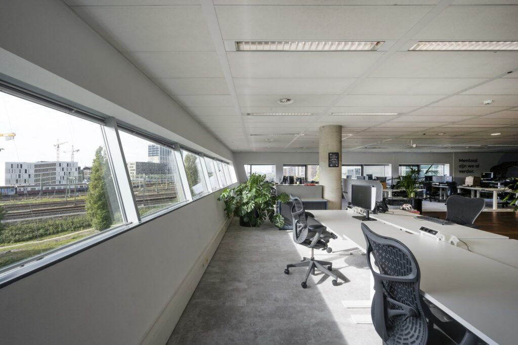 Modern kantoorinterieur in Rietlandpark met uitzicht op spoorlijnen en bebouwing buiten de ramen.
