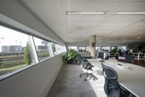 Modern kantoorinterieur in Rietlandpark met uitzicht op spoorlijnen en bebouwing buiten de ramen.