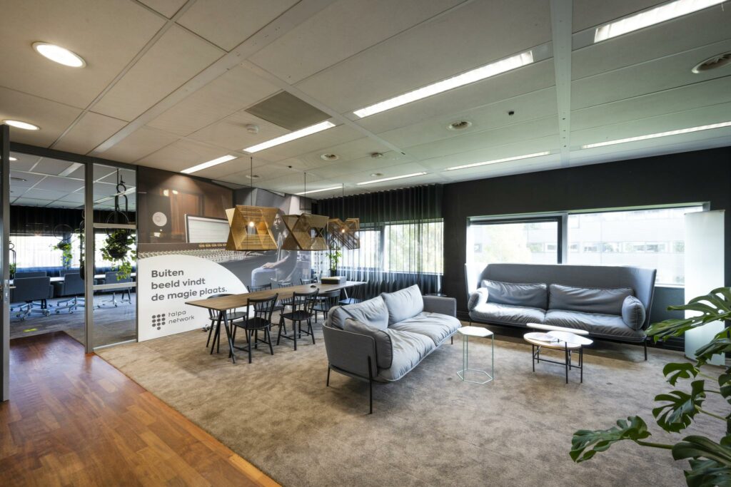 Moderne loungeruimte op kantoor Rietlandpark met comfortabele zitbanken, vergadertafel en decoratieve verlichting.