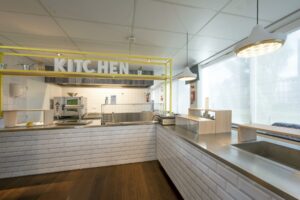 Moderne, lichte keuken met witte tegels, rvs-aanrecht en gele accenten in Rietlandpark.