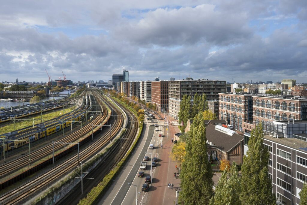 Luchtfoto van Rietlandpark in Amsterdam met treinsporen, woongebouwen en een drukke weg.