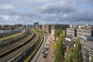 Luchtfoto van Rietlandpark in Amsterdam met treinsporen, woongebouwen en een drukke weg.