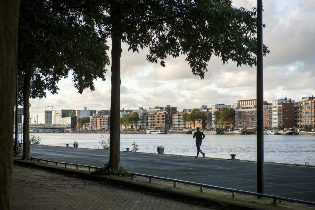 Jogger rent langs het water bij Rietlandpark met uitzicht op moderne gebouwen aan de overkant.