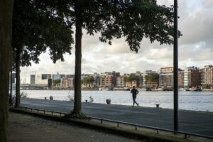 Jogger rent langs het water bij Rietlandpark met uitzicht op moderne gebouwen aan de overkant.