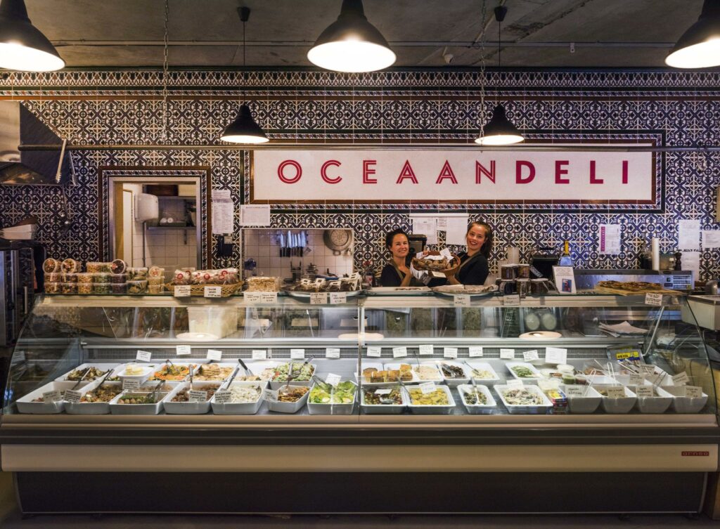 Twee medewerkers achter de toonbank van Oceaan Deli in Rietlandpark met een vitrine vol mediterrane delicatessen.
