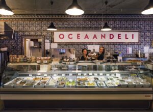 Twee medewerkers achter de toonbank van Oceaan Deli in Rietlandpark met een vitrine vol mediterrane delicatessen.