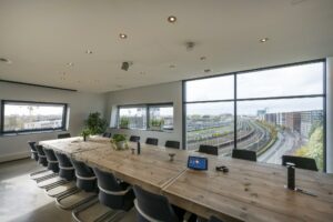 Vergaderruimte met houten tafel en uitzicht op spoor en gebouwen in Rietlandpark, Amsterdam.