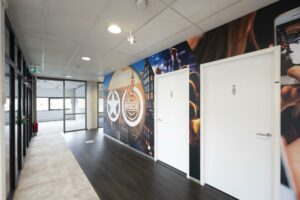 Moderne gang met witte toiletten en een kleurrijke muurfoto met het logo van Rietlandpark 6 Inside.