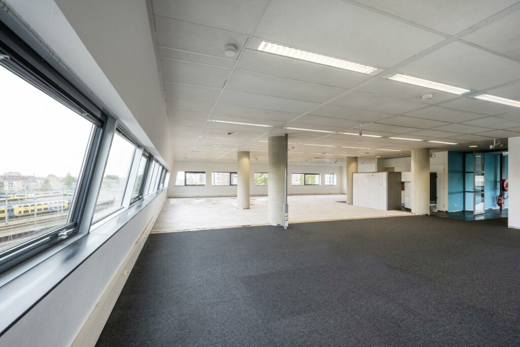 Lichte, lege kantoorruimte in Rietlandpark met grote ramen en zicht op het spoor.
