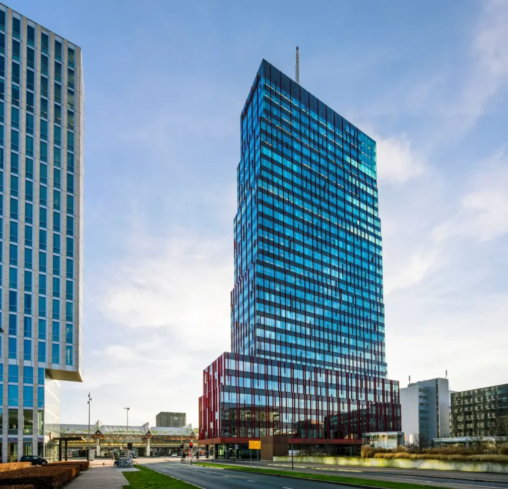 Modern high-rise building on P.J. Oudweg in Almere with a red lower section and blue-tinted glass facade.