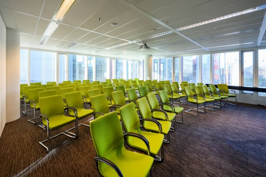 Modern conference room at P.J. Oudweg with rows of green chairs and large windows letting in natural light.