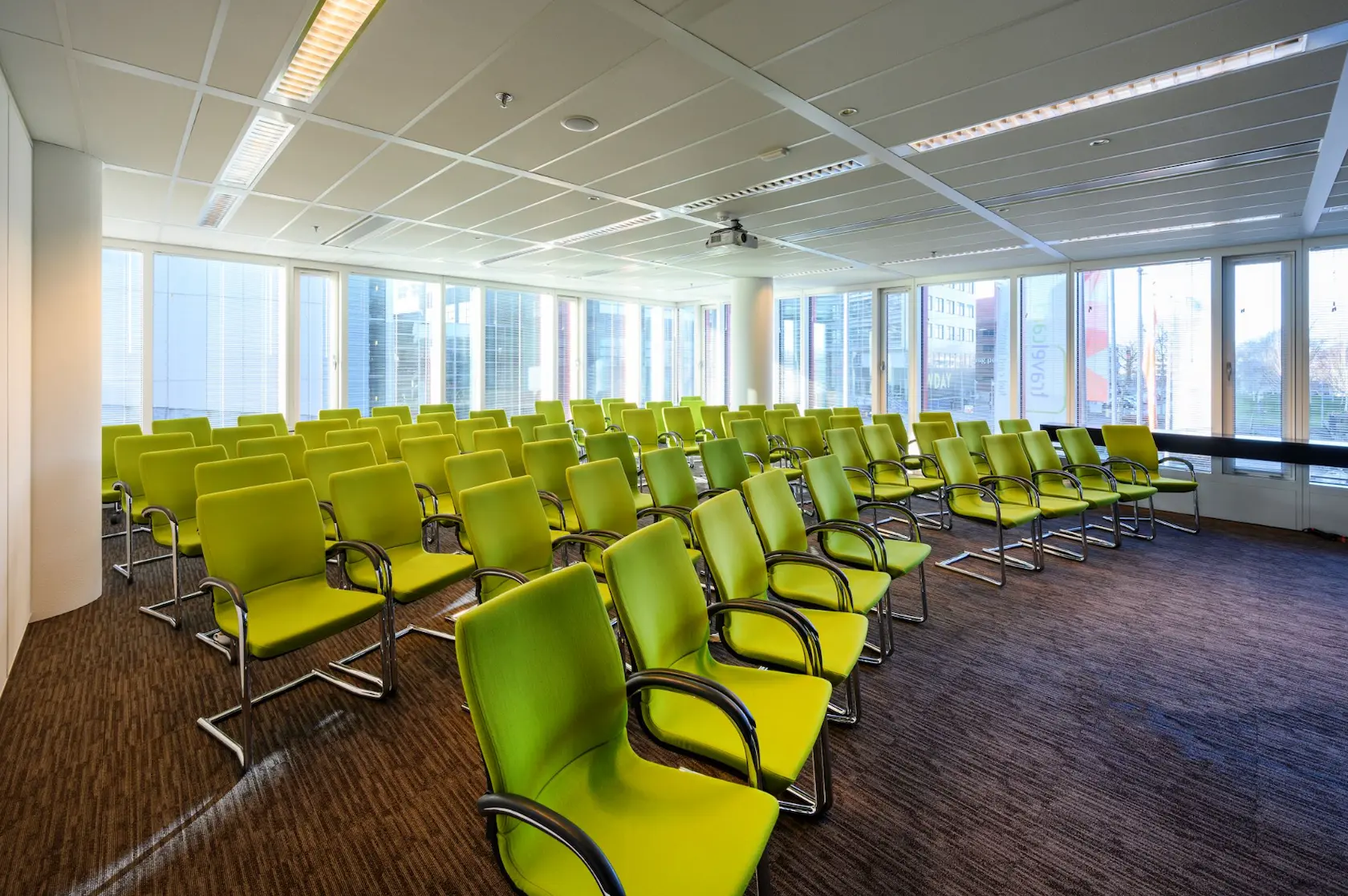 Modern conference room at P.J. Oudweg with rows of green chairs and large windows letting in natural light.
