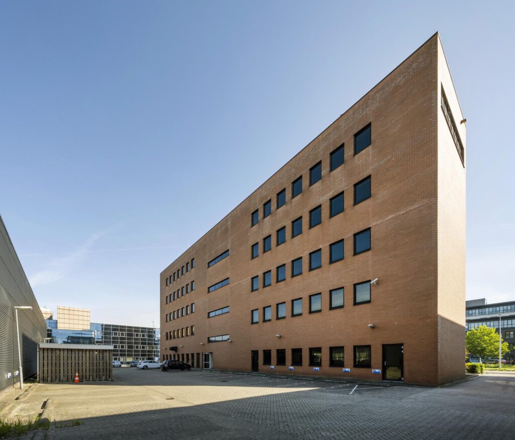 Bakstenen kantoorgebouw aan de Paasheuvelweg met meerdere verdiepingen en zwarte raamkozijnen, gefotografeerd vanaf de parkeerplaats.
