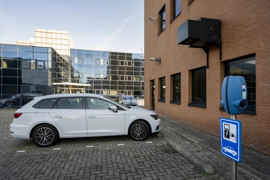 Witte auto staat geparkeerd bij een oplaadpunt naast een kantoorpand aan de Paasheuvelweg.