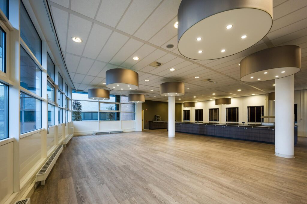 Lichte, moderne zaal aan de Paasheuvelweg met houten vloer, grote ramen en ronde plafondlampen.