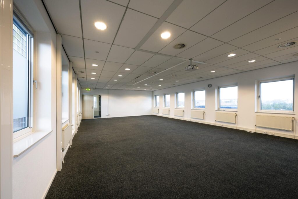 Leeg kantoorruimte aan de Paasheuvelweg met systeemplafond, ramen rondom en grijze vloerbedekking.