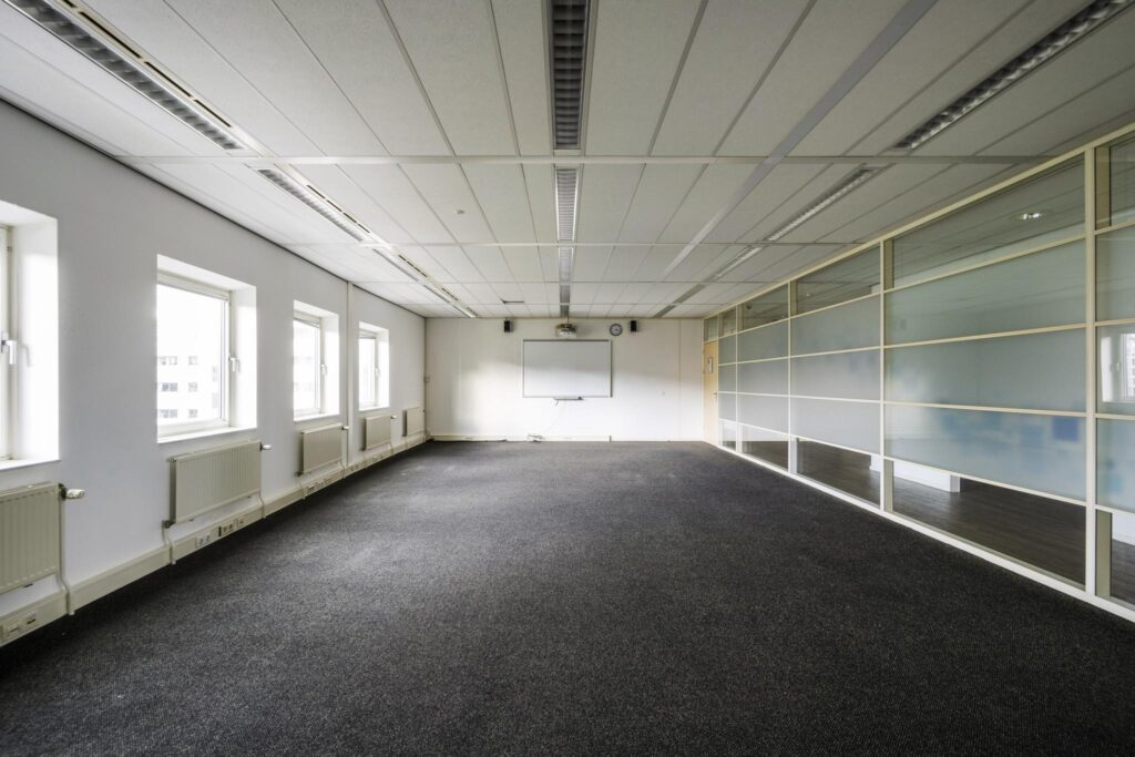 Leeg kantoorruimte aan de Paasheuvelweg met tapijtvloer, systeemplafond, whiteboard en glazen scheidingswand.