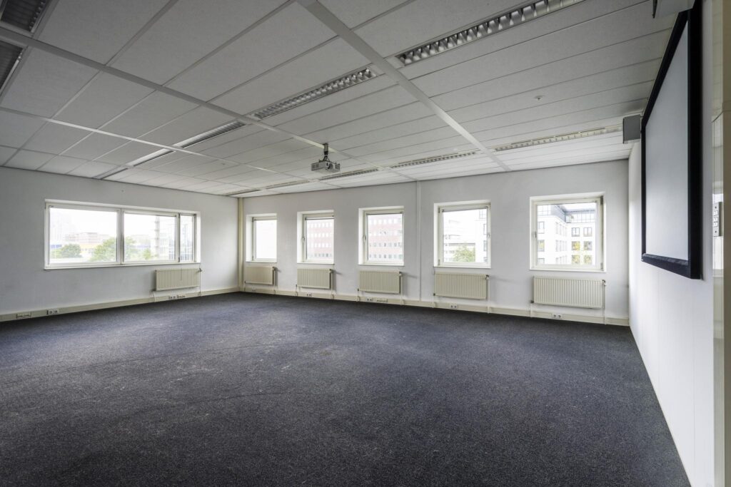 Lege kantooruimte aan de Paasheuvelweg met vijf ramen, projector en projectiescherm.