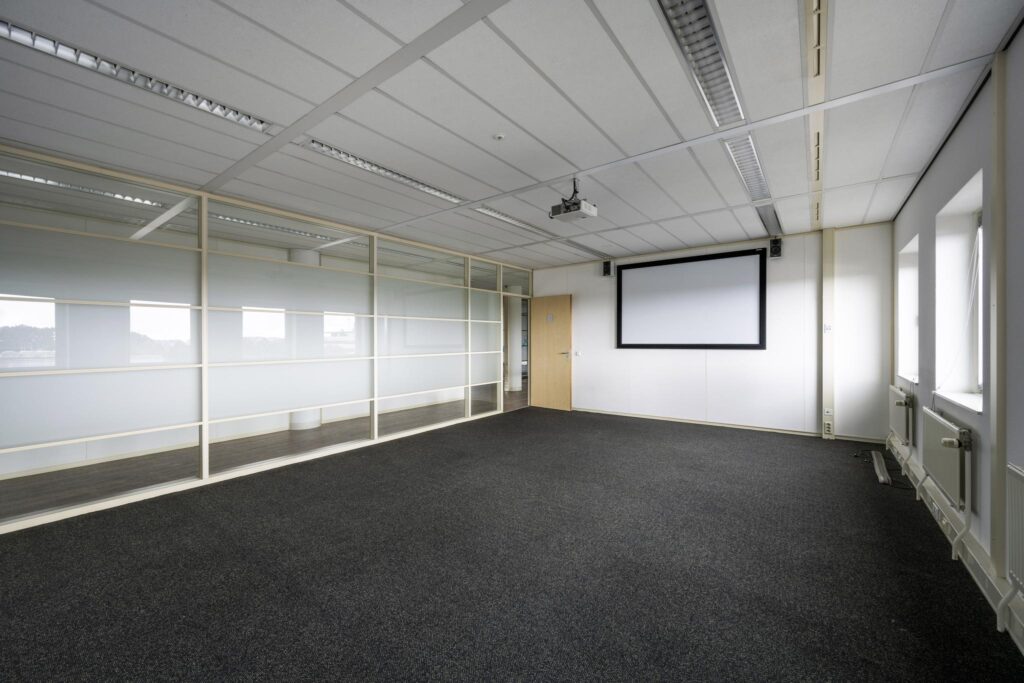 Lege vergaderruimte aan de Paasheuvelweg met tapijtvloer, glazen tussenwand, projectiescherm en plafondbeamer.