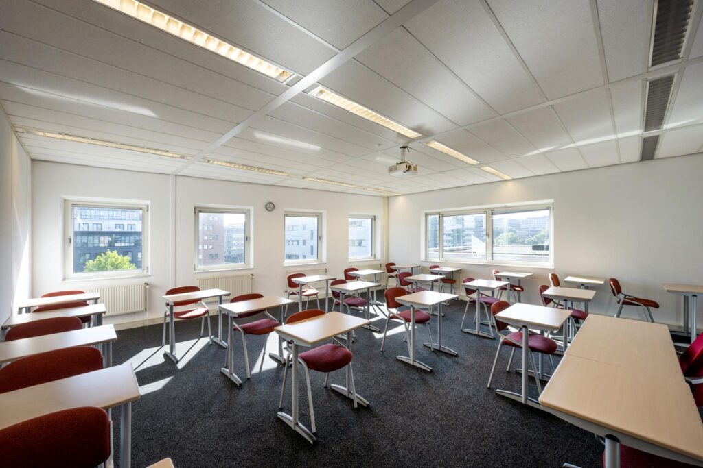 Licht en modern klaslokaal aan de Paasheuvelweg met rode stoelen en losse bureaus.